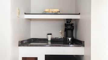 Une cuisine équipée d’un plan de travail, d’une machine à café, d’une prise électrique et d’une pile de livres sur une étagère.