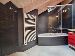 A modern bathroom with a bathtub, a glass shower enclosure, dark tiled walls, and a wooden ceiling. - Chateau B41 by Interhome (Saas-Fee)