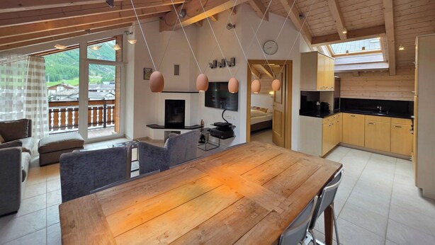 Ein geräumiger Wohnbereich mit einem Holzesstisch, grauen Sofas und einem an der Wand befestigten Fernseher.