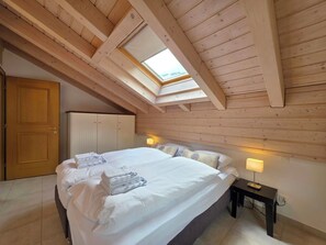 Een slaapkamer met dakraam, een bed met handdoeken, een nachtkastje en een kledingkast.
