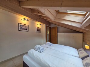 Ein Schlafzimmer mit zwei Betten, Holzbalkendecke und einem Oberlicht.
