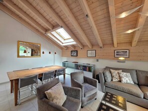 Ein modernes Interieur mit Holzboden, Dachfenstern, einer Essecke, Sitzgelegenheiten und einem Bücherregal.