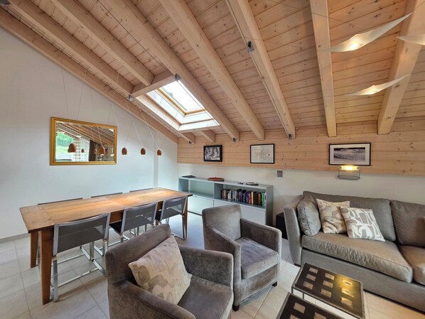 Een modern interieur met houten plafond, dakramen, een eethoek, zitplaatsen en een boekenkast.