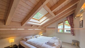Ein Schlafzimmer mit einem großen Bett, einem Nachttisch, einer Lampe, einem Fenster mit Vorhängen und einem Dachfenster.