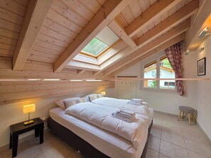 Ein Schlafzimmer mit einem großen Bett, einem Nachttisch, einer Lampe, einem Fenster mit Vorhängen und einem Dachfenster.