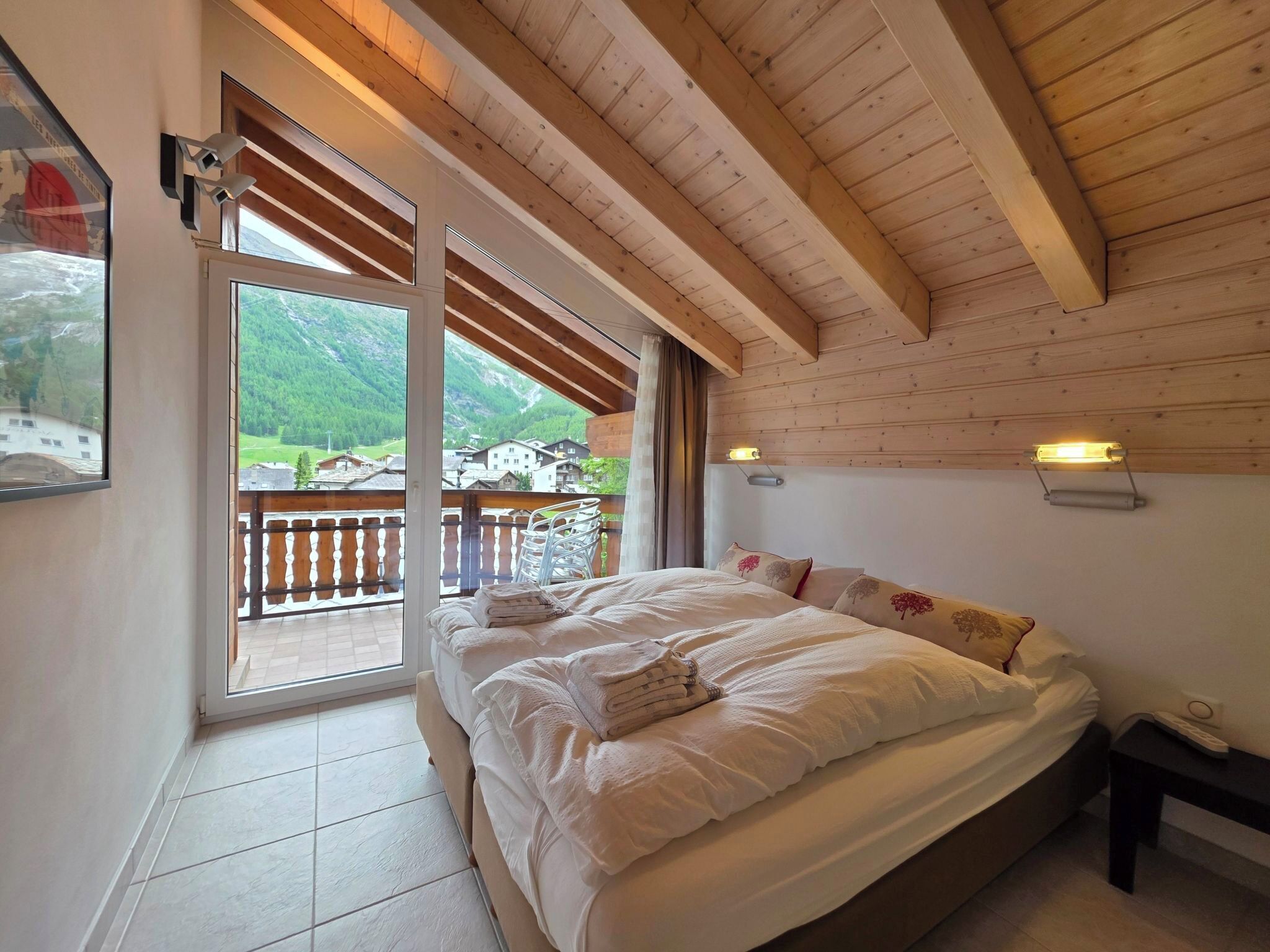 A bedroom with a bed, a window, and a view of a balcony.