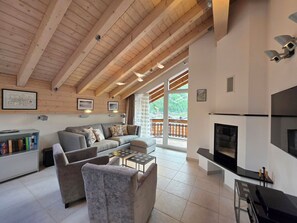 A modern living room with a fireplace, wooden ceiling beams, and a large window overlooking a balcony. - Chateau B41 by Interhome (Saas-Fee)