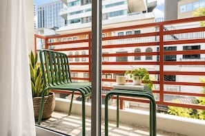 A balcony with two green chairs, a potted plant, and a small table with a book and a mug. - LUMA Phrom Phong (Bangkok)