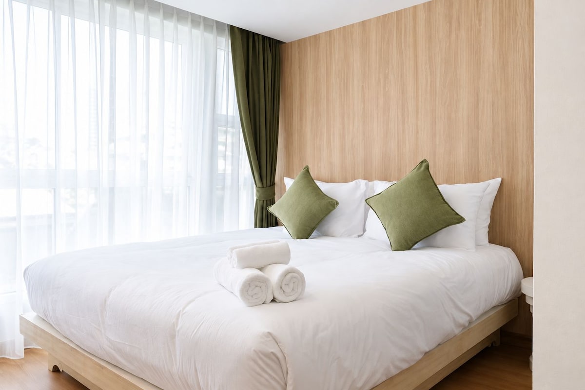 A hotel room with a large bed, white bedding, and green pillows.