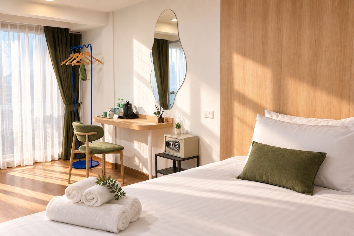 A hotel room with a bed, a desk, a chair, a mirror, and a window with curtains.