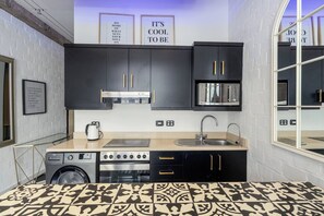 A compact kitchen with a built-in oven, a microwave, and a sink. There are two framed motivational quotes on the wall, and a patterned rug on the floor. - Stylish Temple House Loft by Ctha (Cape Town)