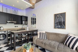 A modern kitchen with a built-in oven, microwave, and sink, a sofa with striped pillows, and a framed abstract painting on the wall. - Stylish Temple House Loft by Ctha (Cape Town)