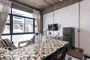 A modern kitchen with a large window, a flat-screen TV, a refrigerator, and a patterned tile floor. - Stylish Temple House Loft by Ctha (Cape Town)