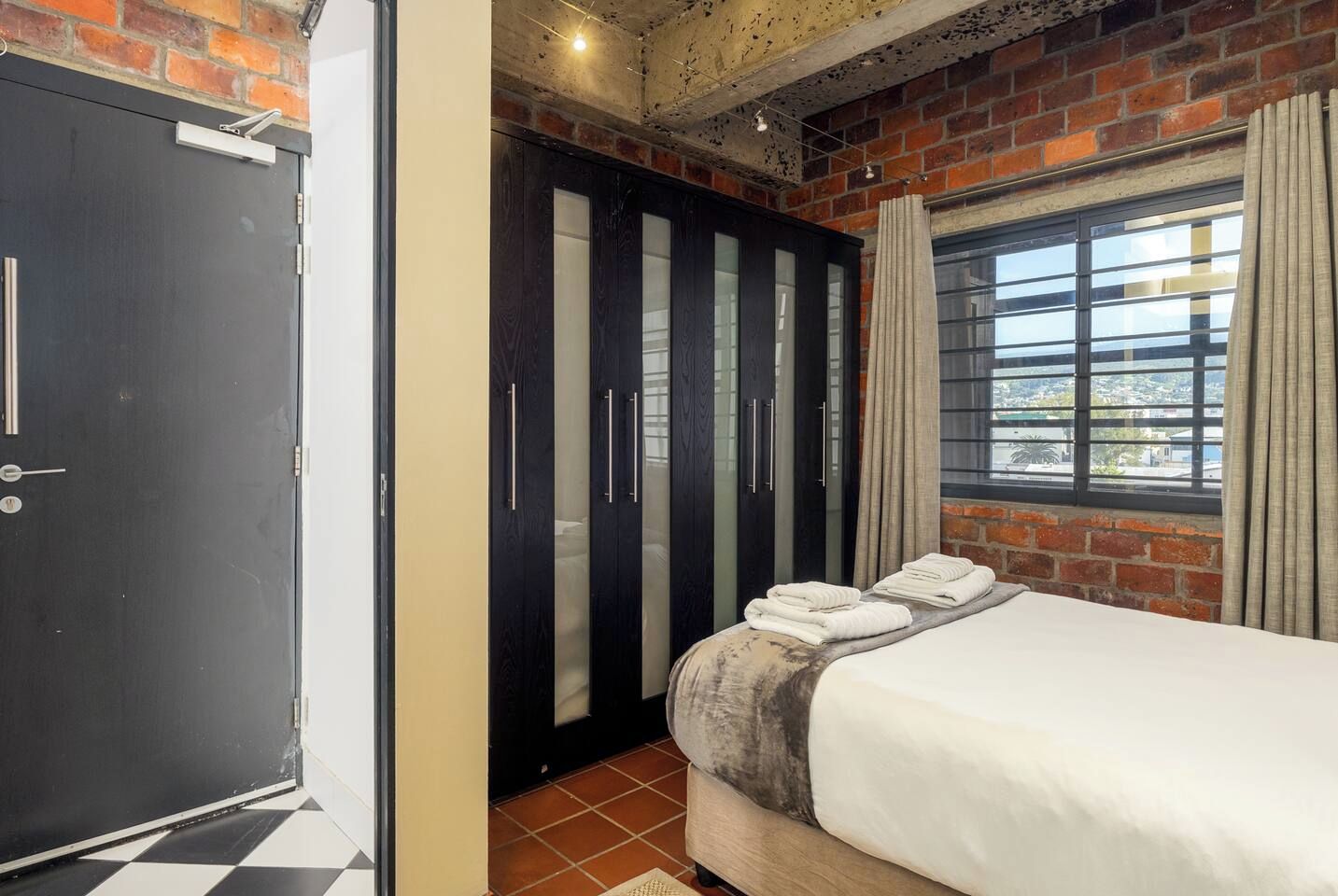 Un dormitorio con cama, armario y ventana con cortinas.