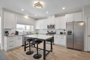 A modern kitchen with white cabinets, a stainless steel refrigerator, and a dining area with a table and chairs. - Luxe Warrenville 4BR | Patio + Pickleball Court (Warrenville)