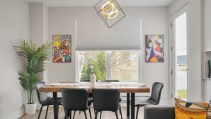 Ein Essbereich mit Holztisch, schwarzen Stühlen, einer Topfpflanze und abstrakten Kunstwerken an den Wänden.