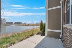 A building with a brick exterior and a window. In the background, there is a body of water with a fountain and a grassy area. - Luxe Warrenville 4BR | Patio + Pickleball Court (Warrenville)