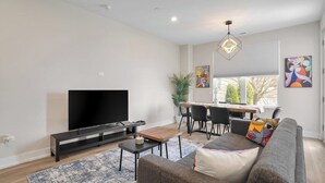 Ein modernes Wohnzimmer mit Flachbildfernseher, einer Couch, einem Couchtisch und einem Essbereich mit Stühlen und einem Tisch.