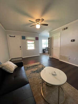 A living room with a black leather sofa, a round white coffee table, a ceiling fan, and a large window. - Renovated Condo: Your home away from home (Decatur)