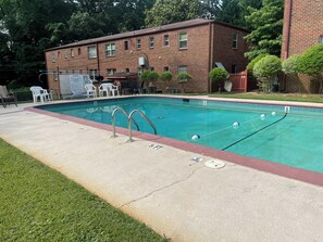 A rectangular swimming pool with a red border, two metal pool ladders, and a poolside area with white chairs and a table.