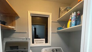 Ein Waschraum mit zwei Waschmaschinen, einem Schild, das darauf hinweist, Handtücher in die Waschmaschine zu legen, und Regalen mit Reinigungsmitteln.
