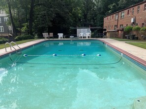A rectangular swimming pool with a clear blue water surface, surrounded by a tiled deck and a brick building. - Renovated Condo: Your home away from home (Decatur)