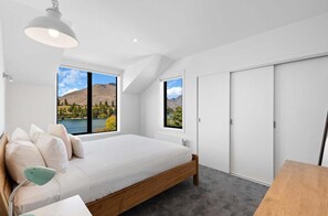A bedroom with a bed, a desk, and a view of a lake and mountains. - 10 The Terrace (Queenstown)
