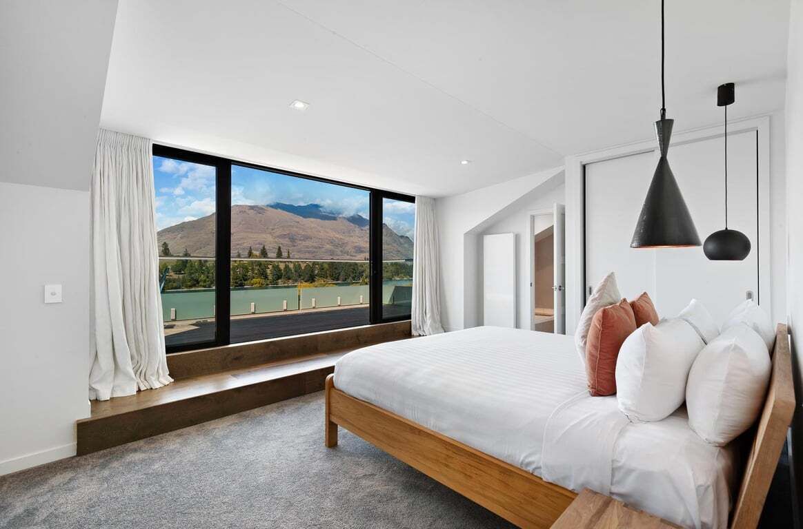 A bedroom with a large window, a bed, and a hanging light fixture.