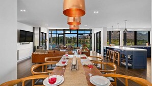 A modern dining area with a wooden table set for four, a large pendant light, and a view of the outdoors. - 10 The Terrace | Lake View | Hot Tub (Queenstown)