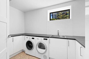 A laundry room with two washing machines, a sink, and a window with a view of greenery. - 10 The Terrace (Queenstown)