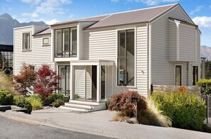 A two-story house with a front porch, large windows, and a mountain backdrop. - 10 The Terrace (Queenstown)