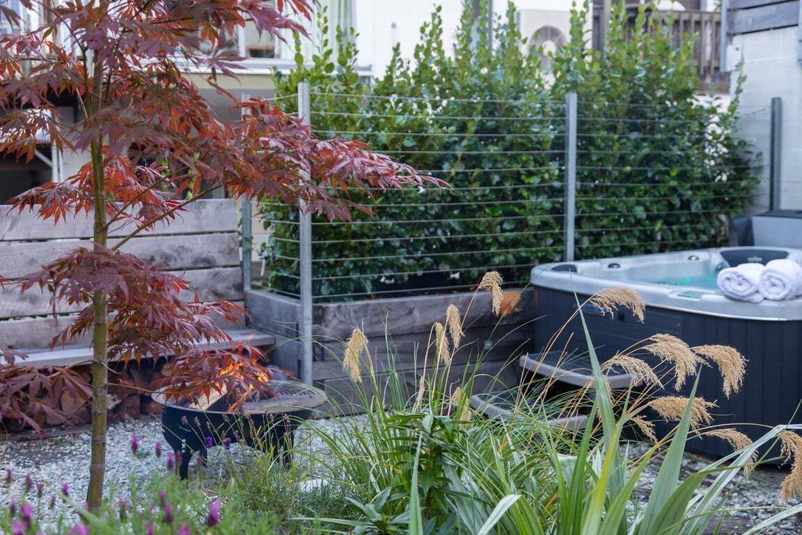 A hot tub surrounded by greenery, a wooden fence, and a stone wall.