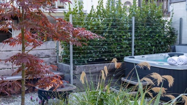 A hot tub surrounded by greenery, a wooden fence, and a stone wall. - 10 The Terrace | Lake View | Hot Tub (Queenstown)