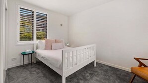A bedroom with a white bed, a small bedside table, a chair, and a window with blinds. - 10 The Terrace | Lake View | Hot Tub (Queenstown)