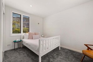A bedroom with a white bed, a small bedside table, a chair, and a window with blinds. - 10 The Terrace | Lake View | Hot Tub (Queenstown)