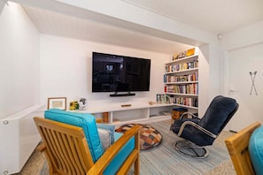A living room with a flat-screen TV, wooden and blue upholstered chairs, a bookshelf, and a patterned rug. - 10 The Terrace (Queenstown)