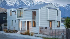 A modern two-story house with a mountain backdrop, featuring large windows and a sloped roof. - 10 The Terrace | Lake View | Hot Tub (Queenstown)