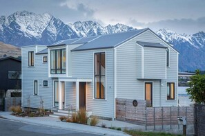 A modern two-story house with a mountain backdrop, featuring large windows and a sloped roof. - 10 The Terrace | Lake View | Hot Tub (Queenstown)