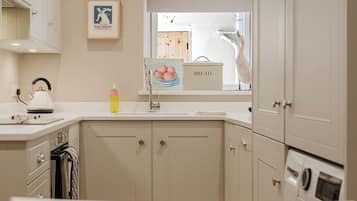 A kitchen with white cabinets, a clock, and a window with a view of the outside.
