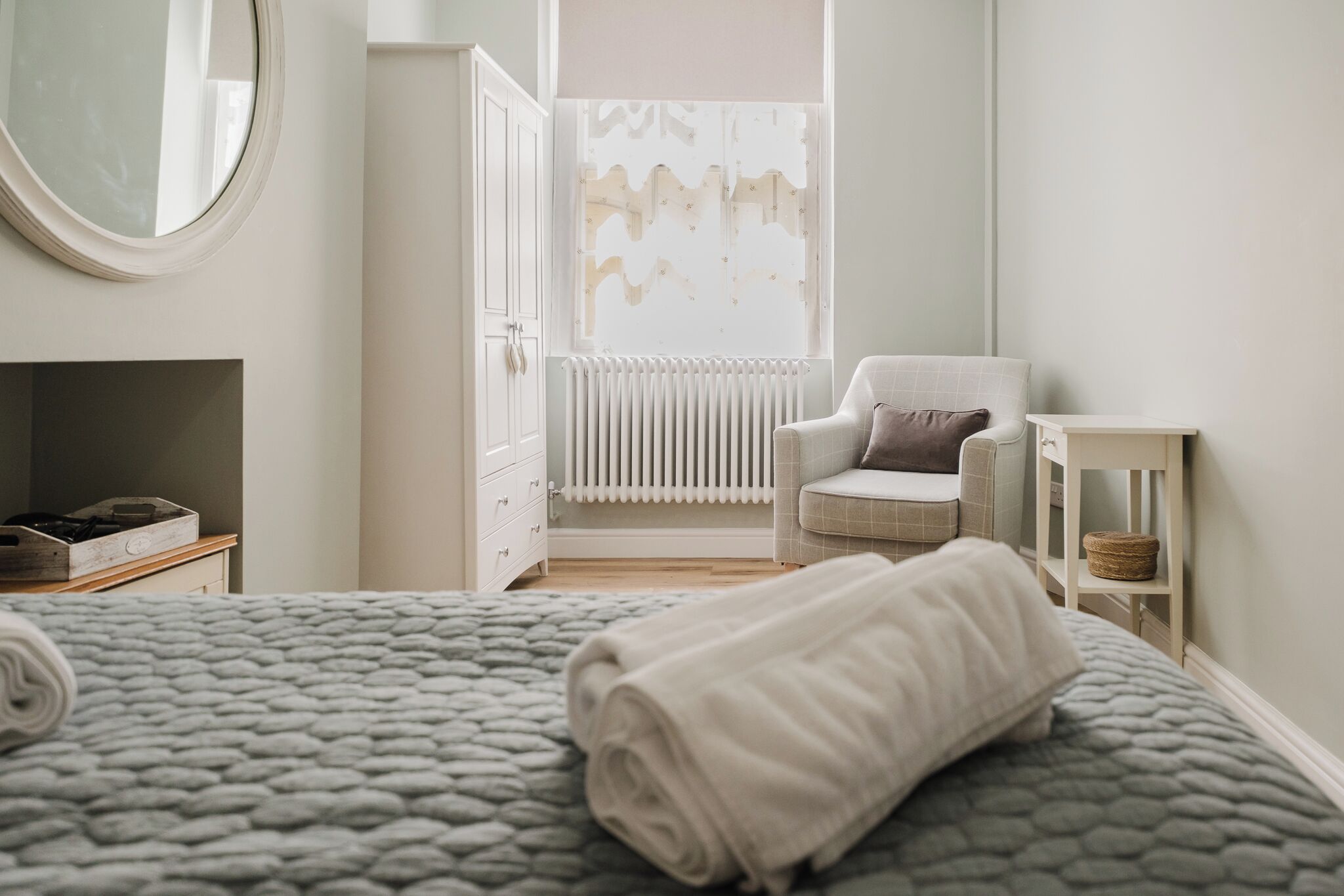 A bedroom with a bed, a chair, a small table, and a radiator.