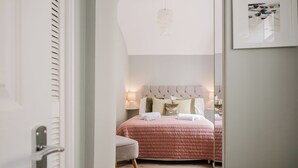 A bedroom with a bed, bedside lamps, a chair, and a mirror. - Stunning Flat in Heart of Cheltenham (Cheltenham)