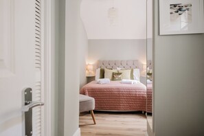 Ein Schlafzimmer mit Bett, Nachttischlampen, einem Sessel und einem Spiegel.