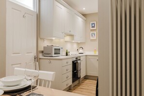 A compact kitchen with white cabinets, a microwave, a kettle, and a dining area with a table set for two. - Stunning Flat in Heart of Cheltenham (Cheltenham)