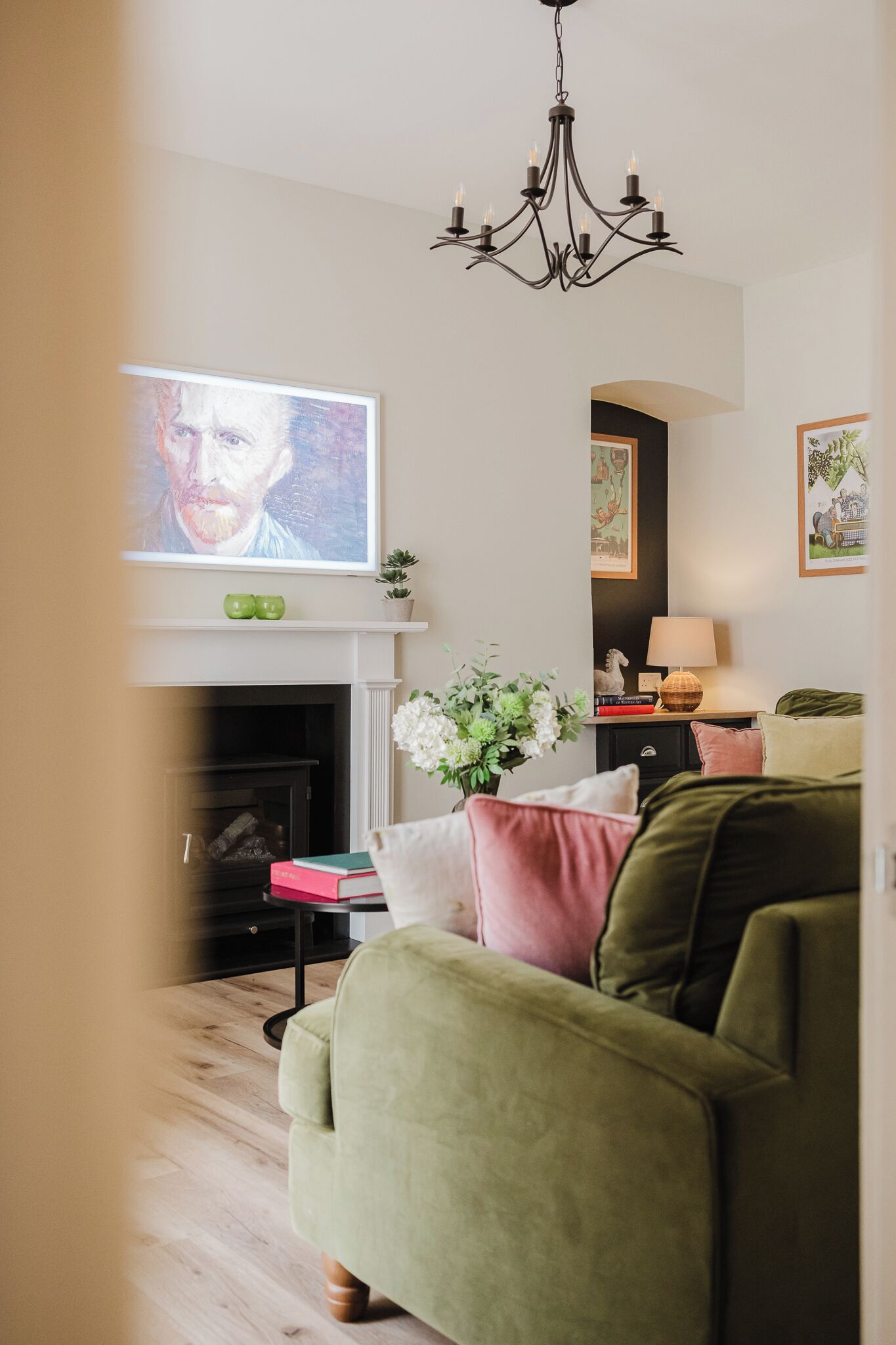 A living room with a green sofa, a fireplace, a television, and a chandelier.