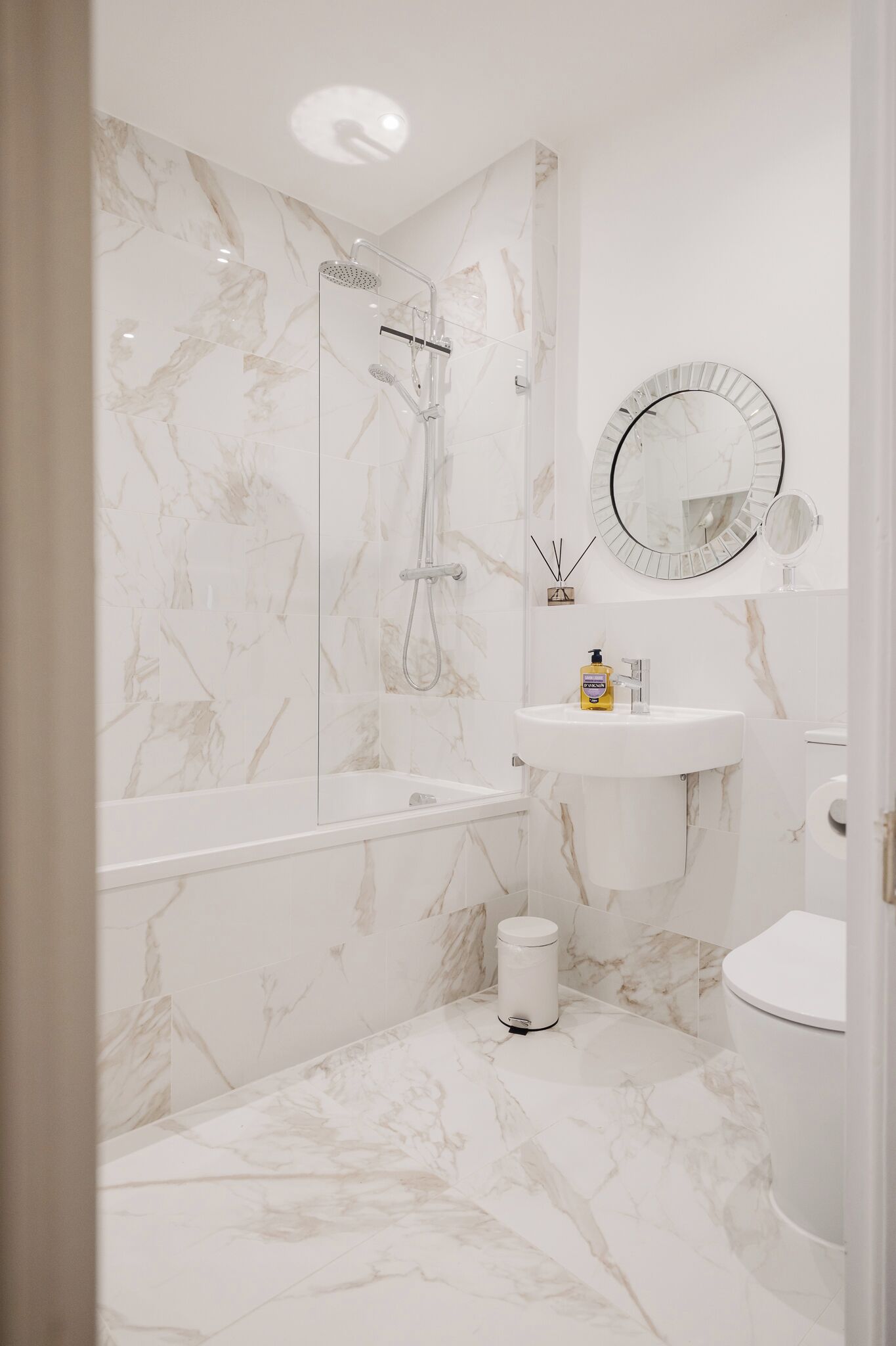Een badkamer met een marmeren douche, wastafel, toilet en spiegel.