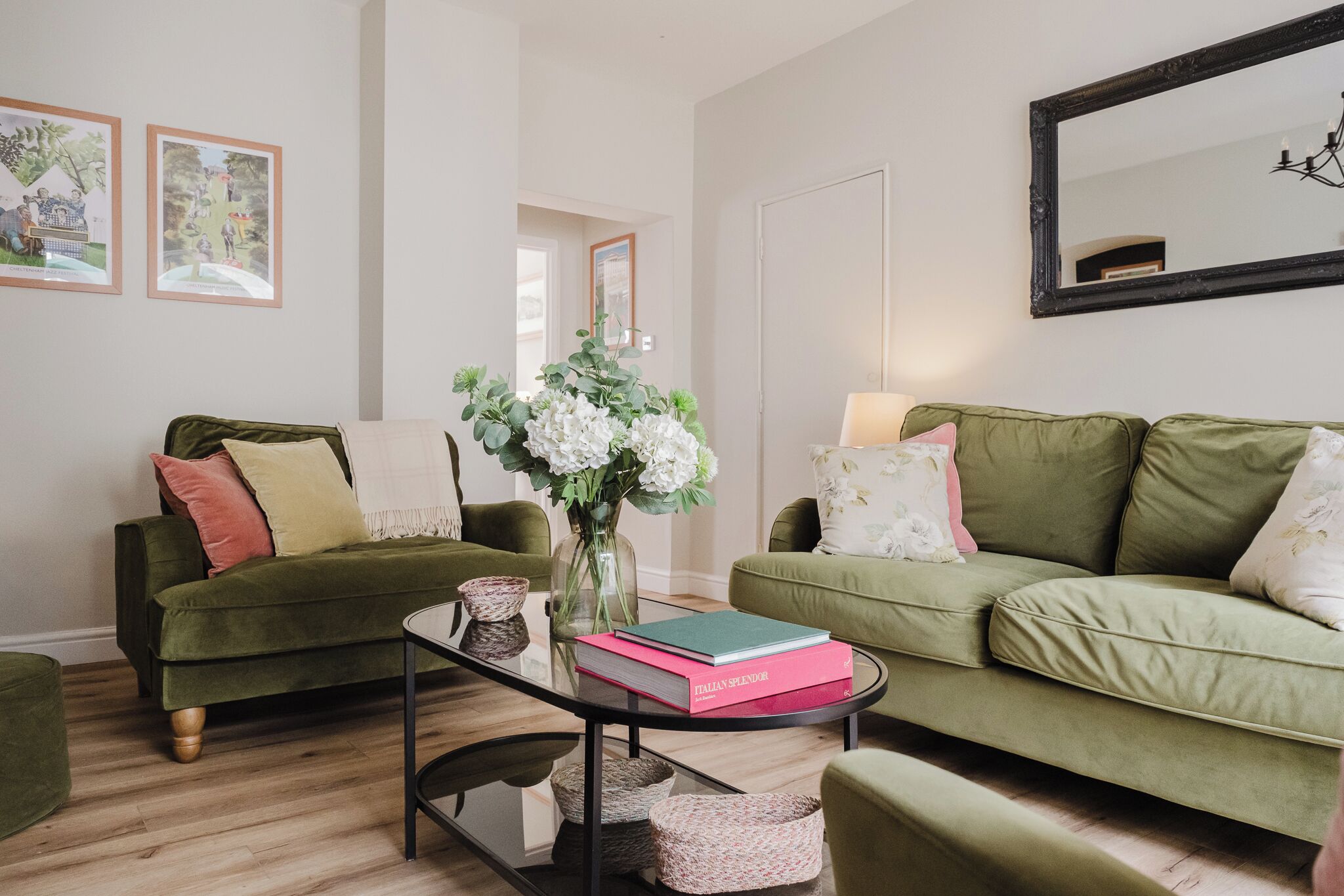 A living room with two green sofas, a glass coffee table, and a vase with flowers.
