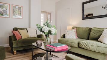 A living room with two green sofas, a glass coffee table, and a vase with flowers.