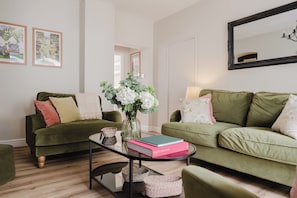A living room with two green sofas, a glass coffee table, and a vase with flowers. - Stunning Flat in Heart of Cheltenham (Cheltenham)
