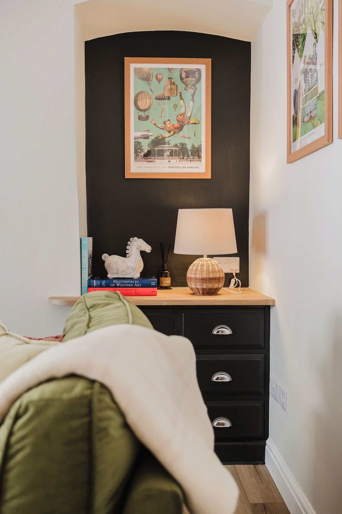 A bedroom with a bed, a nightstand with books, a lamp, and a framed picture on the wall.