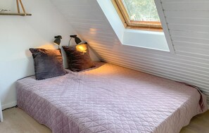 Ein Einzelbett mit gesteppter Bettdecke, zwei Wandleuchten und ein Oberlicht in einem Raum mit weißen Wänden und Holzbalken.